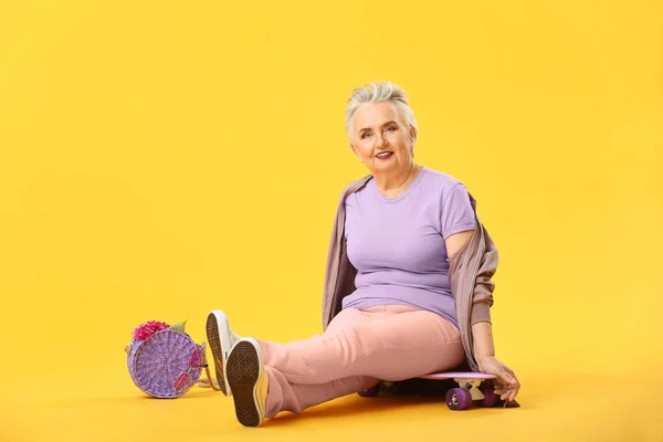 Elegante donna anziana con skateboard su sfondo colore — Foto Stock