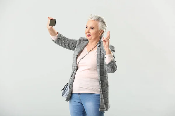 Stijlvolle oudere vrouw die selfie op lichte achtergrond neemt — Stockfoto