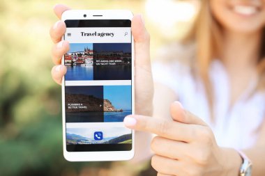 Seyahat acentesi web sitesinin açık sayfası ile cep telefonu tutan kadın