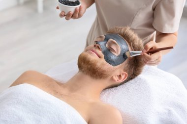 Kozmetik uzmanı spa salonunda adamın yüzüne maske takıyor.