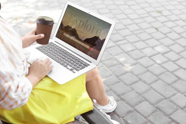 Mulher com laptop visitando site agência de viagens enquanto sentado no banco ao ar livre — Fotografia de Stock