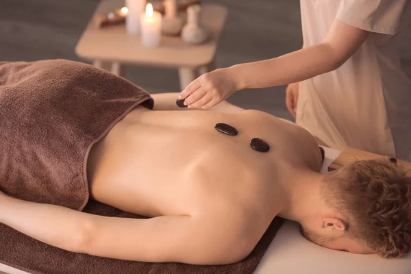 Handsome young man undergoing treatment with spa stones in beauty salon — Stock Photo, Image