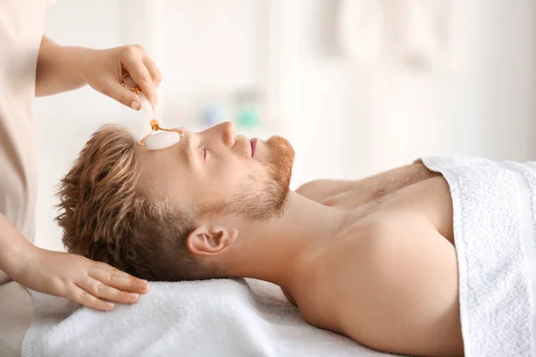 Bonito jovem recebendo massagem facial no salão de spa — Fotografia de Stock