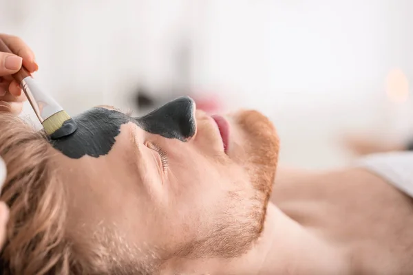 Cosmetólogo aplicando máscara en la cara del hombre en el salón de spa — Foto de Stock