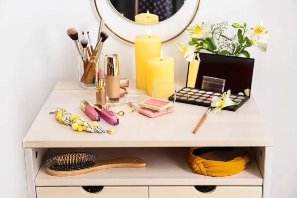 Cosméticos de maquiagem com escovas e jóias na mesa de vestir no quarto — Fotografia de Stock