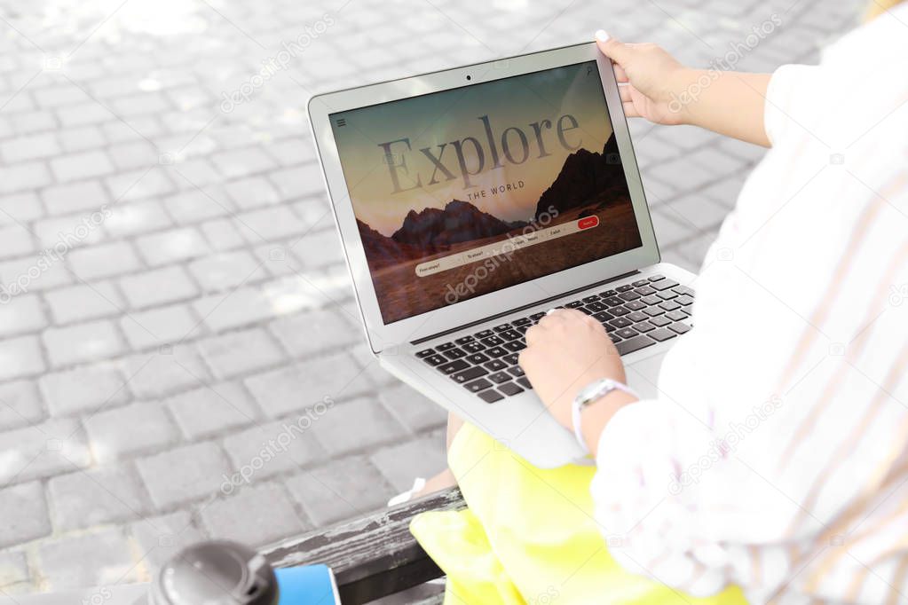 Woman with laptop visiting travel agency website while sitting on bench outdoors