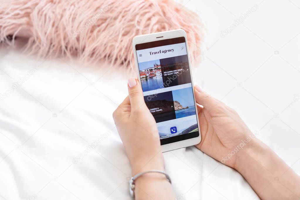 Woman with mobile phone visiting travel agency website at home