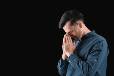 Dindar adam karanlık arka planda Tanrı 'ya dua ediyor.