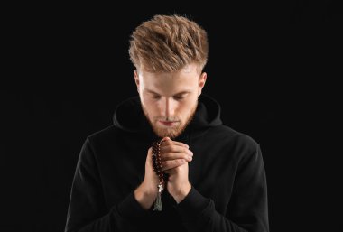 Dindar genç adam karanlık arka planda Tanrı 'ya dua ediyor.