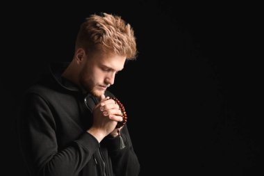 Dindar genç adam karanlık arka planda Tanrı 'ya dua ediyor.