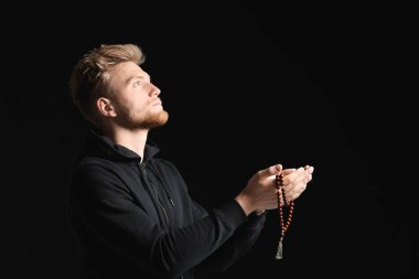Dindar genç adam karanlık arka planda Tanrı 'ya dua ediyor.