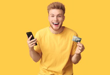 Renkli arka planda kredi kartı ve cep telefonu ile Mutlu genç adam