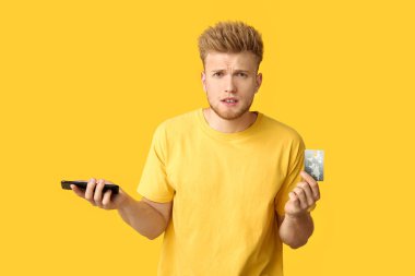 Renkli arka planda kredi kartı ve cep telefonu ile stresli genç adam