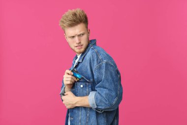 Şüpheli genç adam renkli arka plan ceket cebine kredi kartı koyarak