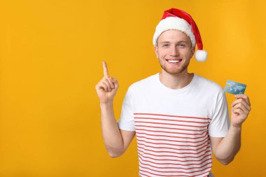 Santa şapka mutlu genç adam ve renkli arka plan üzerinde kredi kartı ile