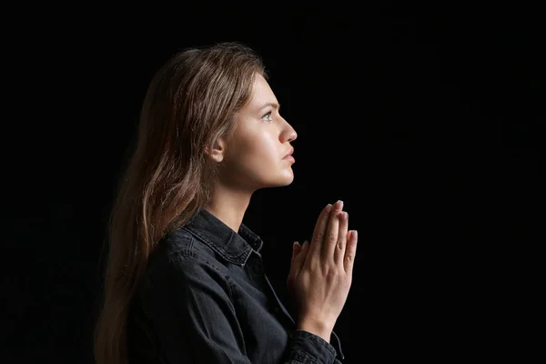 Religiöse junge Frau betet vor dunklem Hintergrund zu Gott — Stockfoto