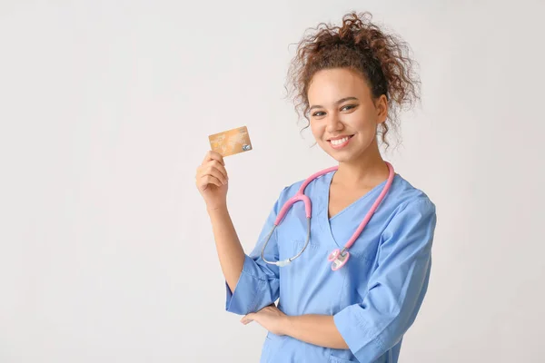 Médico afro-americano com cartão de crédito em fundo claro — Fotografia de Stock