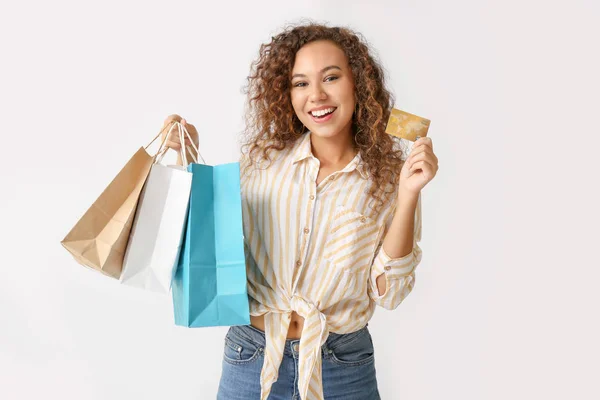 Hermosa mujer afroamericana con tarjeta de crédito y bolsas de compras sobre fondo claro —  Fotos de Stock