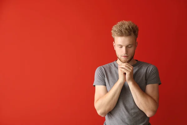 Religious young man praying to God on color background — Stock Photo, Image