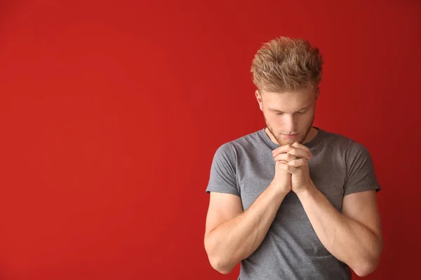 Religious young man praying to God on color background — Stock Photo, Image