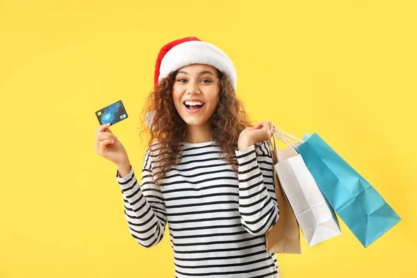 Felice donna afro-americana in cappello Santa, con carta di credito e borse della spesa su sfondo colore — Foto Stock
