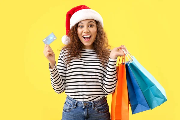 Happy African-American woman in Santa hat, with credit card and shopping bags on color background — Stock Photo, Image