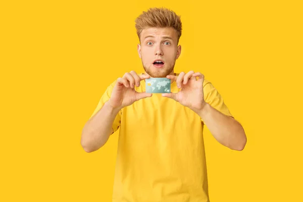 Shocked young man with credit card on color background — Stock Photo, Image