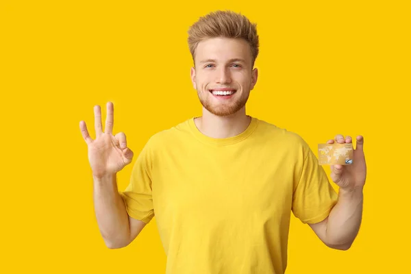 Щасливий молодий чоловік з кредитною карткою показує добре жест на кольоровому фоні — стокове фото
