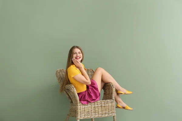 Happy young woman sitting in armchair on color background — Stock Photo, Image