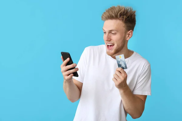 Podekscytowany młody człowiek z kartą kredytową i telefonem komórkowym na tle kolorów — Zdjęcie stockowe