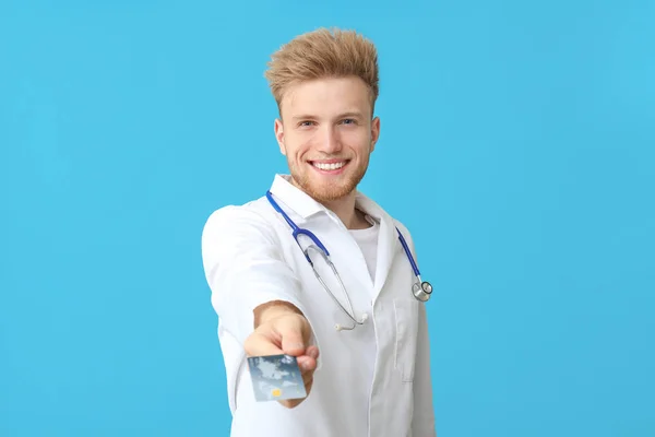 Médico macho feliz com cartão de crédito em fundo de cor — Fotografia de Stock