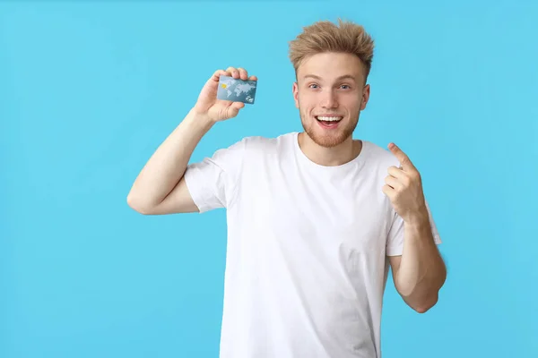 Happy young man with credit card on color background — Stock Photo, Image