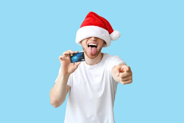 Gelukkige jonge man in kerstmuts en met creditcard op kleur achtergrond — Stockfoto