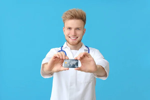 Happy male doctor with credit card on color background — Stock Photo, Image