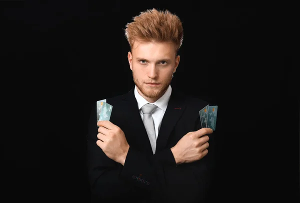 Bonito homem de negócios com cartões de crédito no fundo escuro — Fotografia de Stock