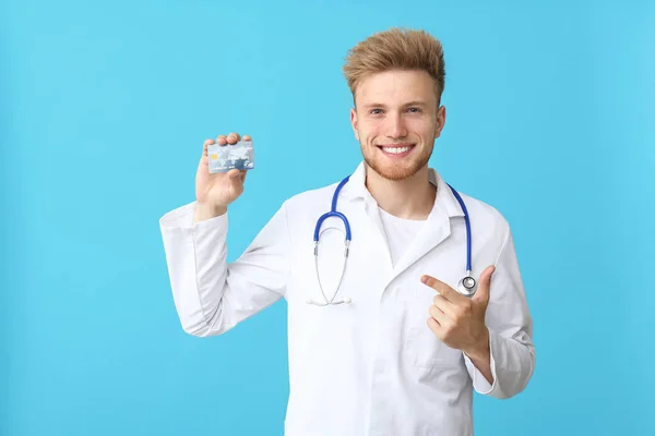 Médico macho feliz com cartão de crédito em fundo de cor — Fotografia de Stock