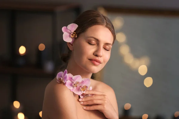 Mulher bonita com flores de orquídea no salão de spa — Fotografia de Stock