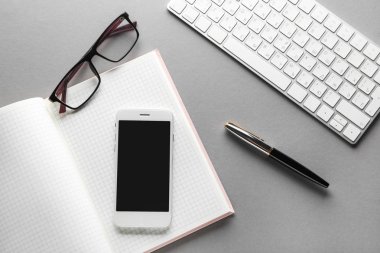 Gri arka planda dizüstü bilgisayar, cep telefonu, gözlük, kalem ve Pc klavye