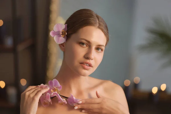 Hermosa joven con flores de orquídea en el salón de spa — Foto de Stock