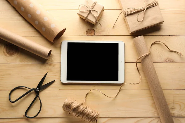 Tablet computer and accessories for packing gifts on wooden background