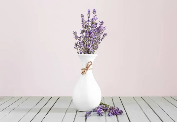 Beautiful lavender flowers in vase on table against light background