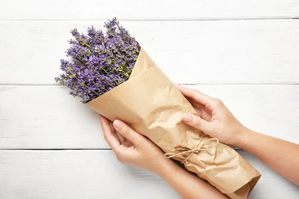 Female hands with bouquet of fresh lavender flowers on white wooden background