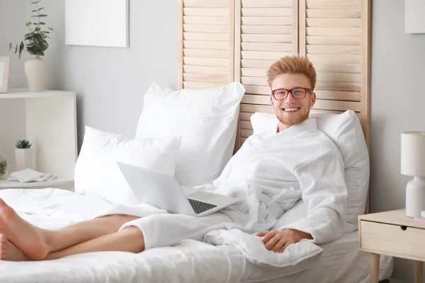寝室にラップトップを持つ若い男の朝 — ストック写真