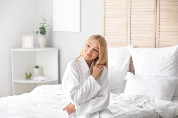 Schöne junge Frau im Bademantel sitzt auf dem Bett — Stockfoto