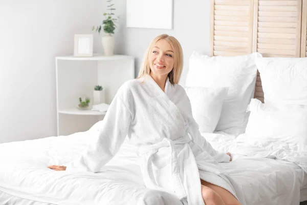 Schöne junge Frau im Bademantel sitzt auf dem Bett — Stockfoto