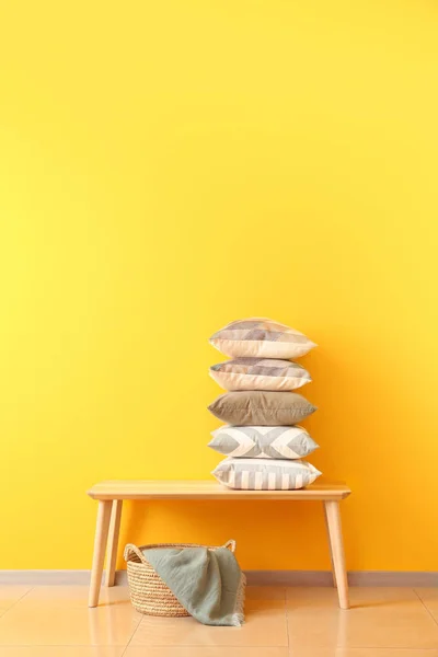 Bord med stack av kuddar och korg nära färg väggen — Stockfoto