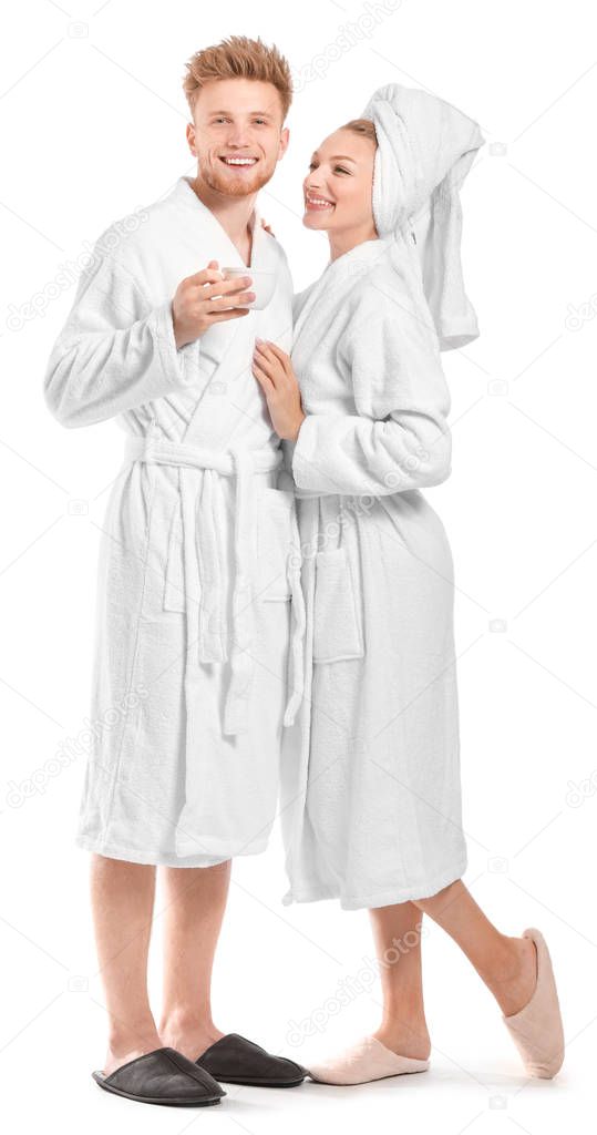 Happy young couple in bathrobes and with cup of coffee on white background