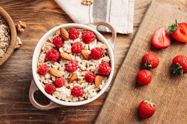 Ahşap masa üzerinde lezzetli tatlı yulaf ezmesi, çilek ve badem ile Pot