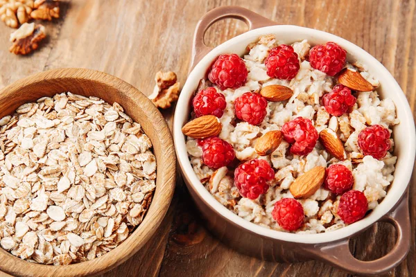 Pot with tasty sweet oatmeal, raspberry and almond on wooden table — Stock Photo, Image