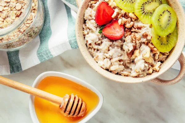 Pot with tasty sweet oatmeal, fruits and honey on light table — Stock Photo, Image